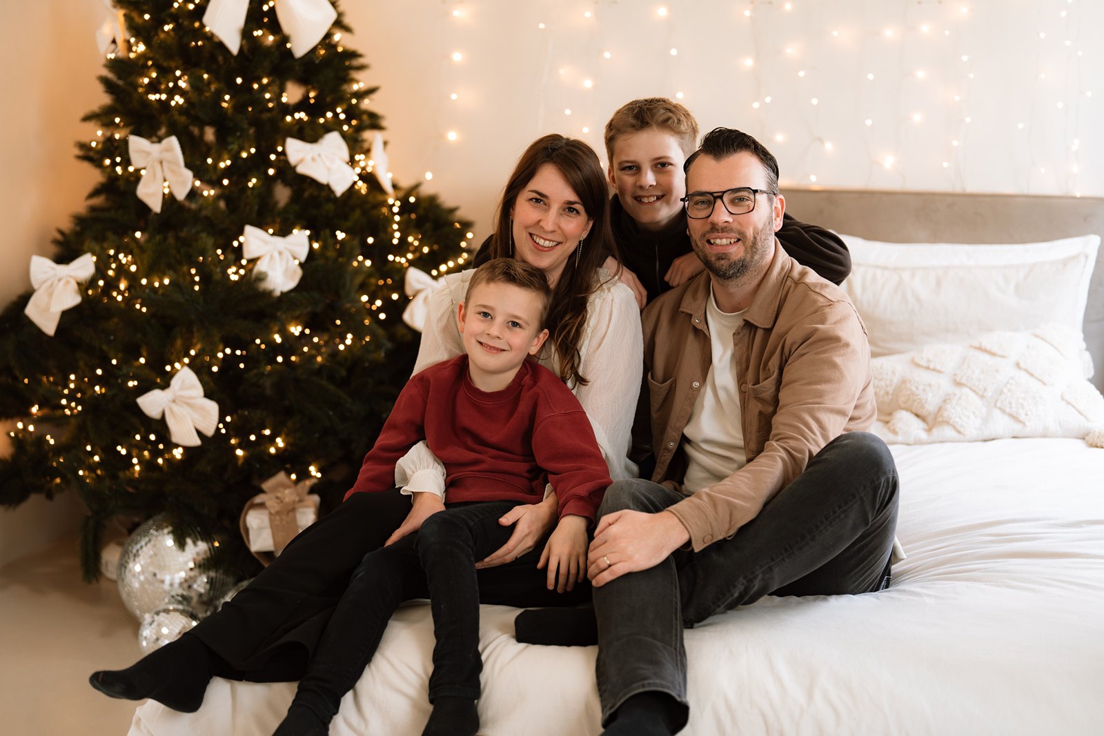 Kerst mini shoot in Gouda van een gezin dat in de studio op bed zit naast de kerstboom.